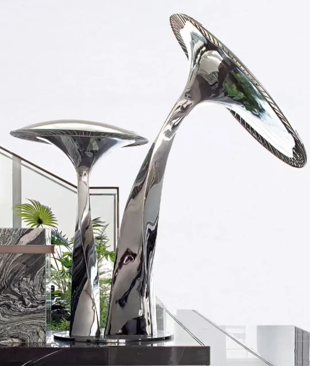 Paired mirror-finish mushroom sculptures shown indoors with an upright stem and a taller curved stem