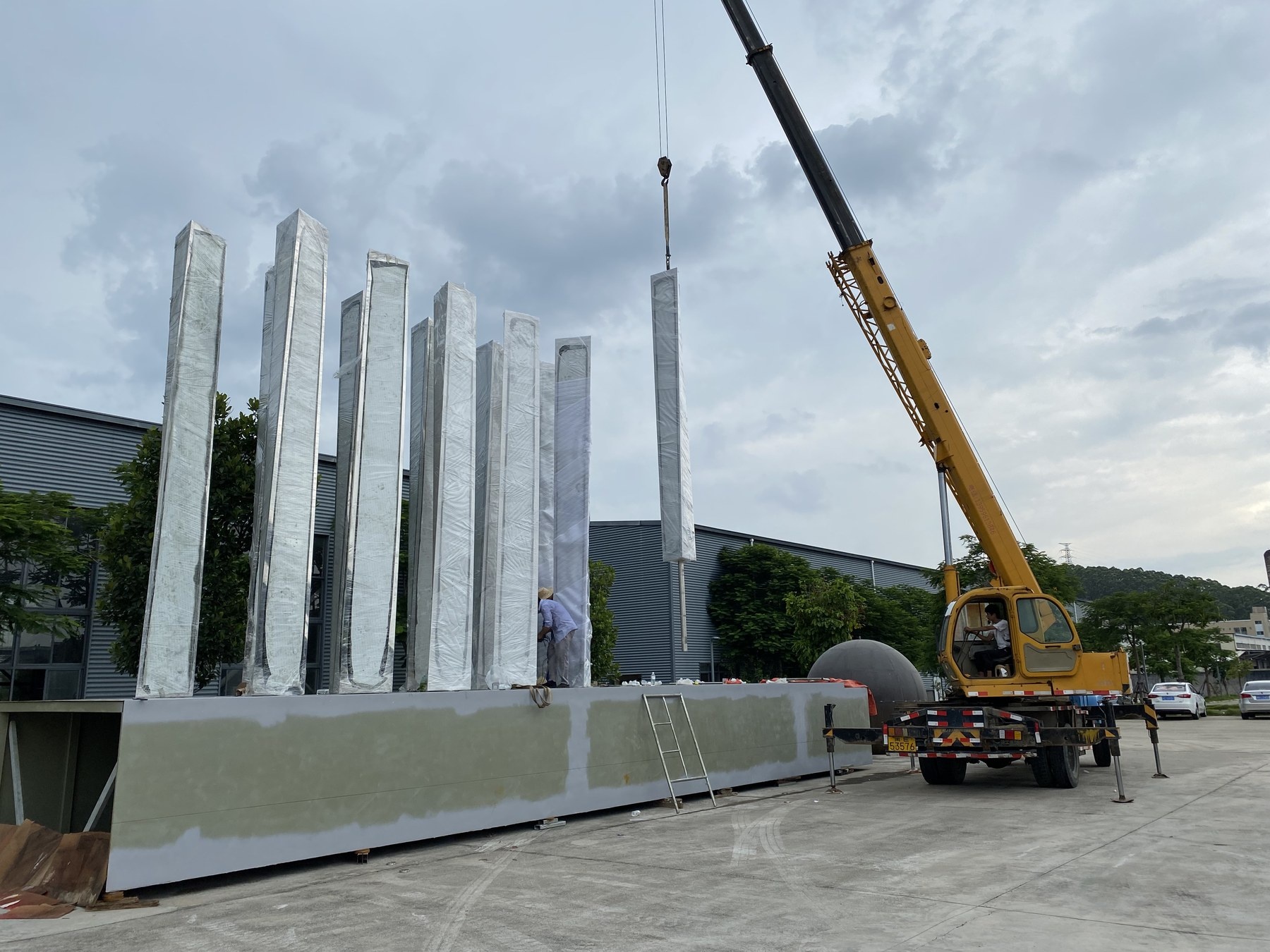 Crane assembly of the same large mirror stainless steel vertical blade sculpture