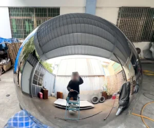 Mirror-polished stainless steel sphere reflecting a workshop, with roof and wall lines curving smoothly