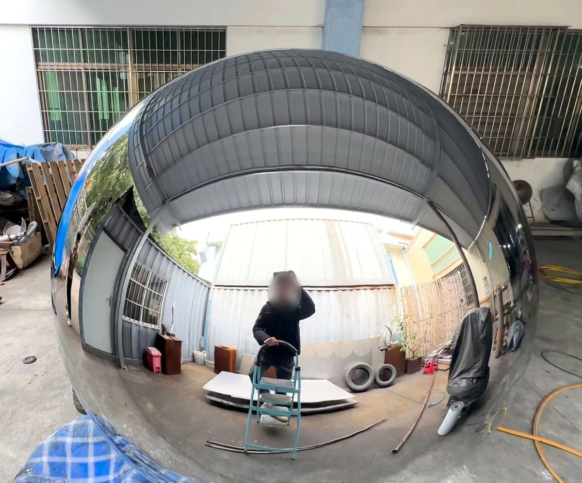 Mirror-polished stainless steel sphere reflecting a workshop, with roof and wall lines curving smoothly