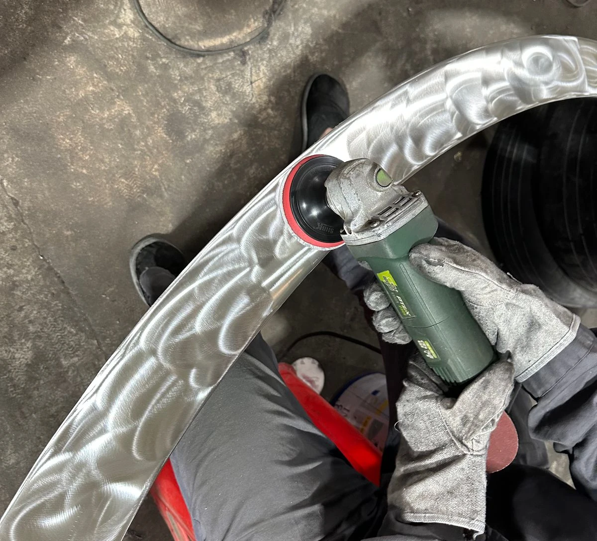 Sanding a stainless steel sculpture band with an angle grinder, leaving swirl marks before polishing