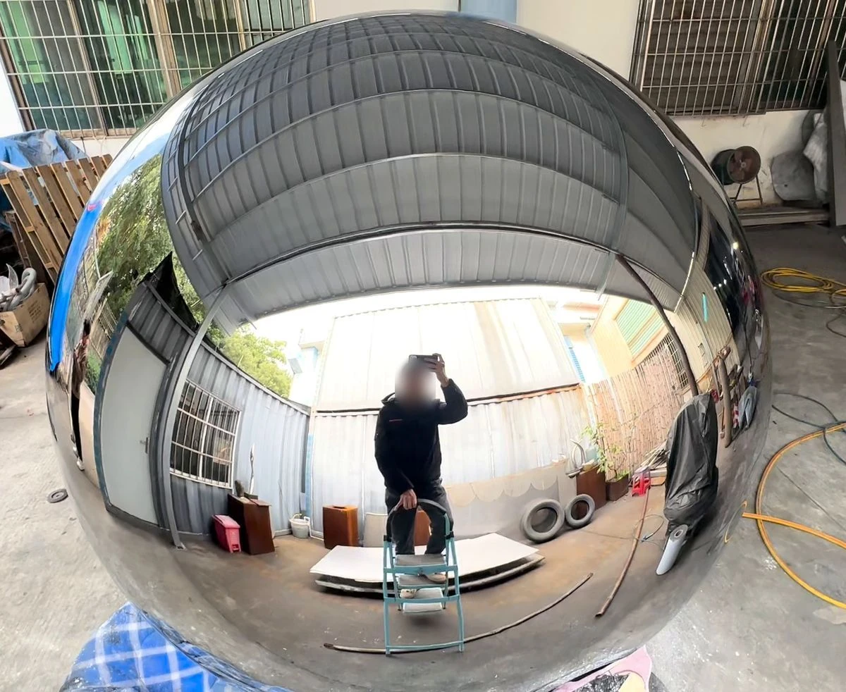 Mirror stainless steel sphere with a continuous reflection: roof lines and walls curve smoothly across the surface